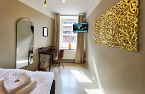Una habitación de hotel con cama, escritorio con silla, televisión y un panel decorativo en la pared.