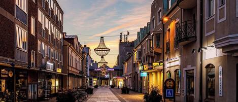 A cobblestone street lined with historic buildings, a central pedestrian path, and a decorative light fixture in the distance.