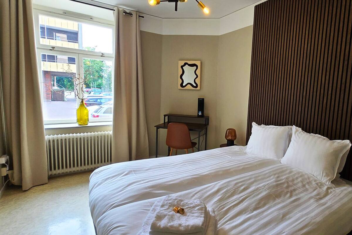 Habitación de hotel con una cama grande, un escritorio y vista a la calle a través de la ventana.