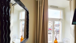 A room with a large mirror, a window with curtains, and a bottle on the windowsill.