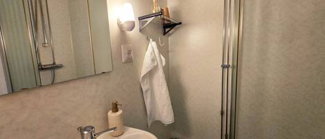 A bathroom with a sink, mirror, towel rack, and a shower area.