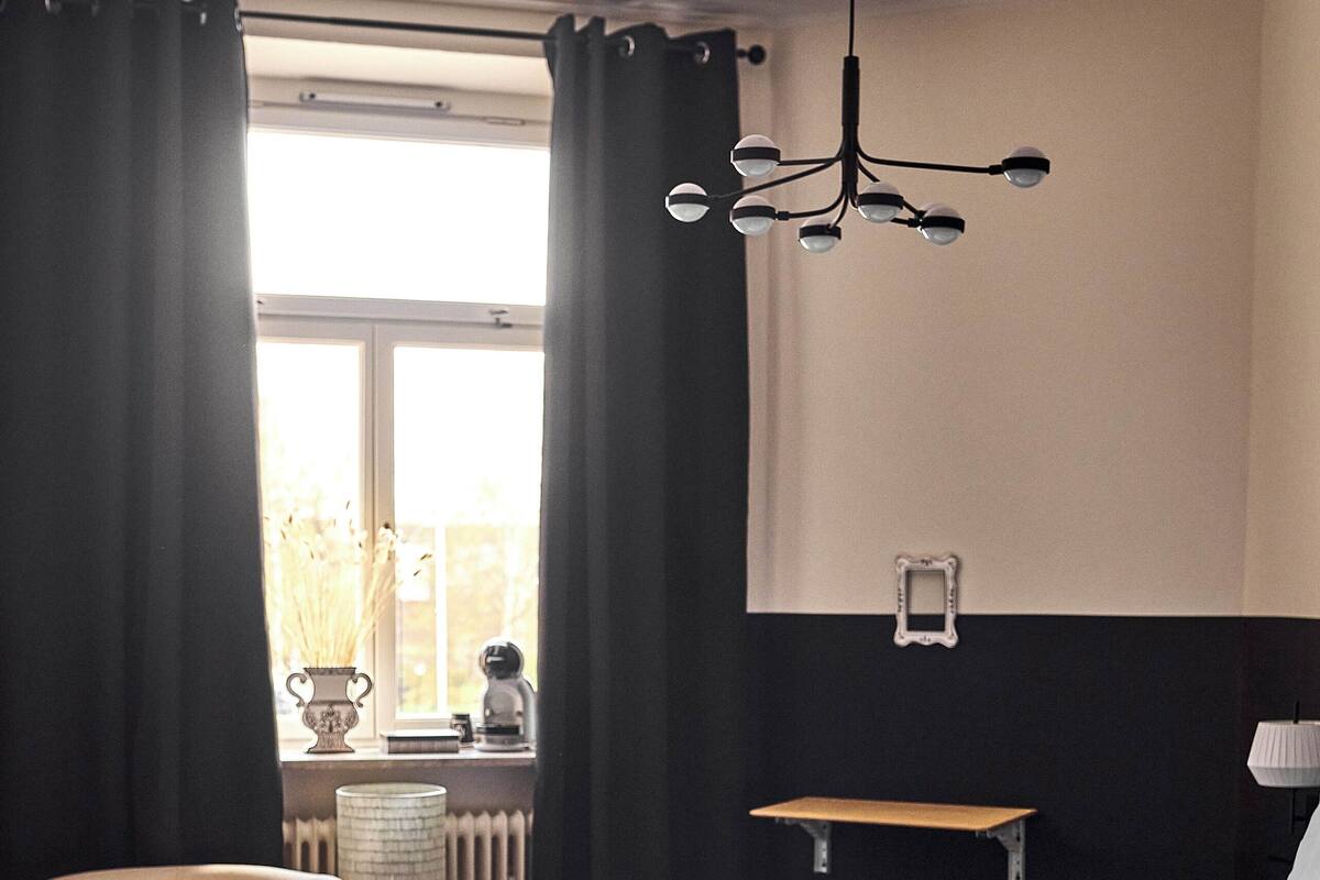 Un dormitorio con cama, una silla, una mesita de noche, una lámpara y un ventanal con cortinas.