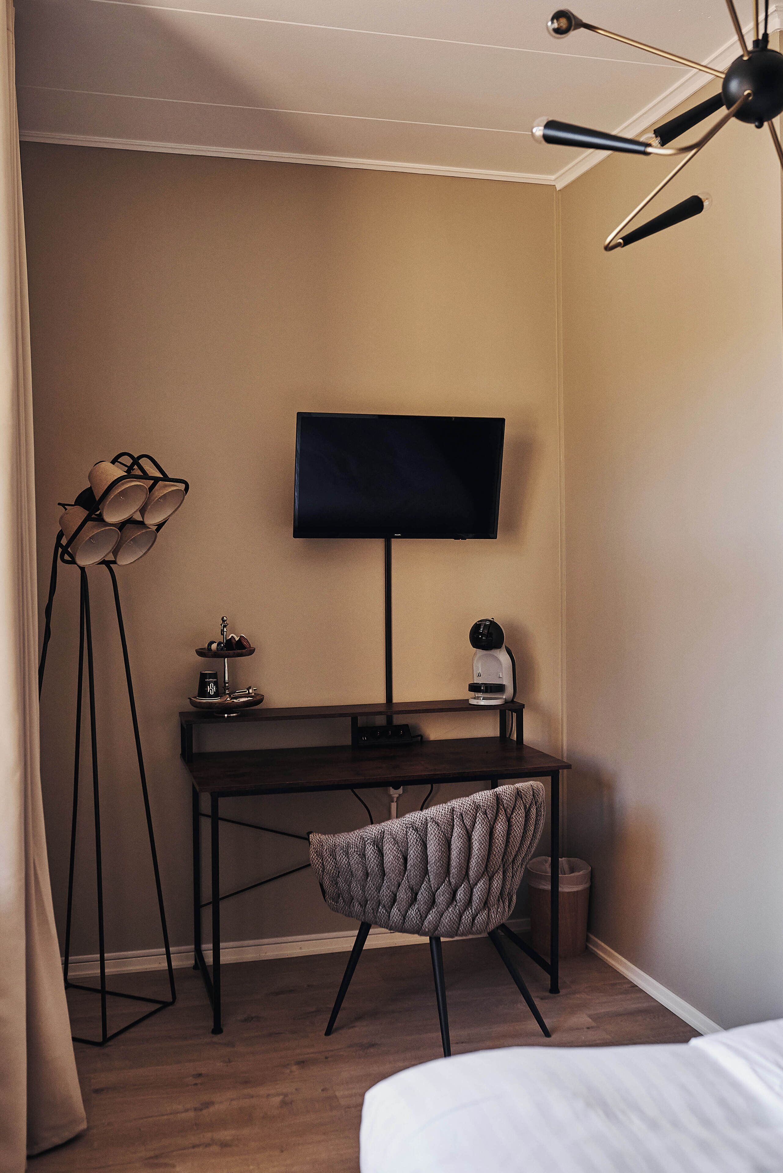 A hotel room with a bed, a desk with a flat-screen TV, a lamp, and a chair.
