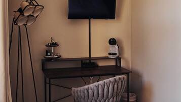 A hotel room with a bed, a desk with a flat-screen TV, a lamp, and a chair.