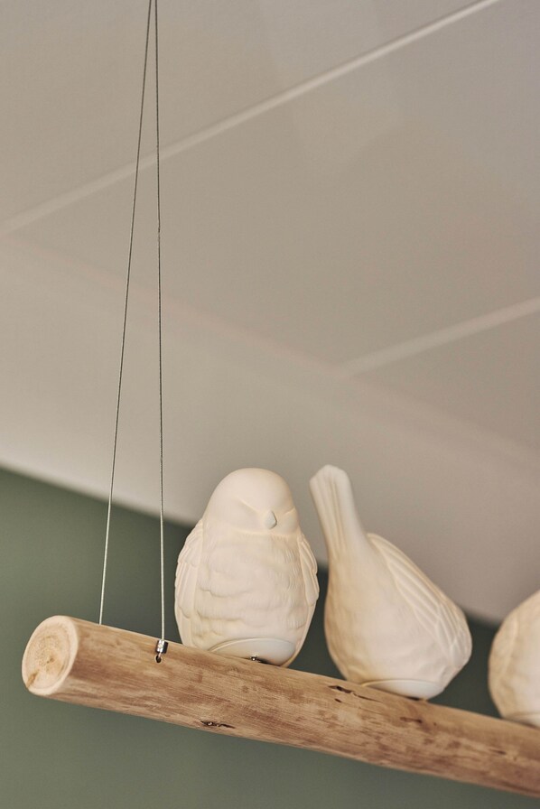 A wooden branch with three white ceramic birds hanging from it.