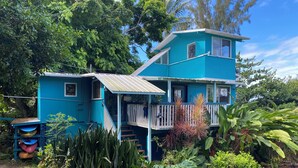A two-story blue house with a balcony, surrounded by lush greenery. - Manta Suite w/ ocean view and sleeping 6 --TA-154-746-2656-01 (Kealakekua)