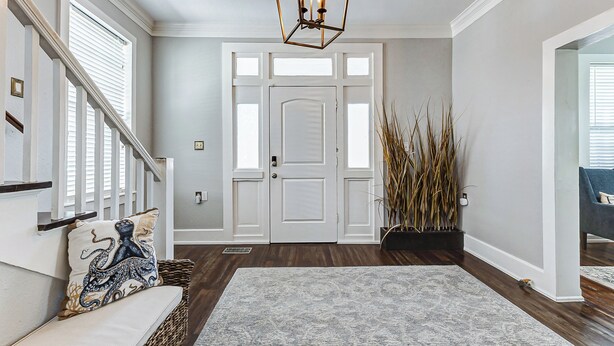 A foyer with a wooden staircase, a white door, a gray rug, and a hanging light fixture. - Modern Oasis Heated Pool, Spa 6 bedroom walk to beach, restaurants, (Galveston)