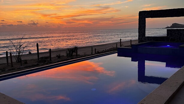 A swimming pool with a view of the sunset over the ocean.
