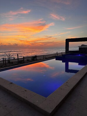 A swimming pool with a view of the sunset over the ocean.