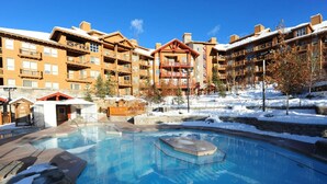 Um resort com piscina, construções de madeira e neve no chão.