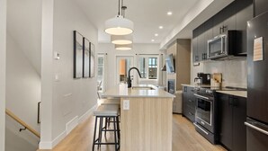 Uma cozinha moderna com ilha central, eletrodomésticos de aço inoxidável e luminária pendente.