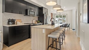 Cozinha moderna com armários escuros, uma ilha central com banquetas e iluminação pendente.