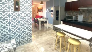 A modern kitchen with a central island, bar stools, and a dining area with a red sofa.