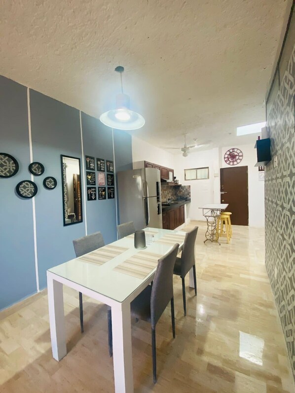 Ein Essbereich mit Tisch und Stühlen, einem Kühlschrank und einer Küche im Hintergrund.