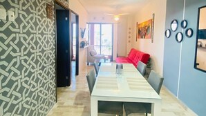 A dining area with a long table, chairs, a red sofa, and a patterned wall.