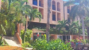 A multi-story building with balconies, surrounded by lush greenery and palm trees.