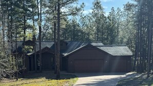 Eine zweistöckige Blockhütte mit Garage, umgeben von hohen Kiefern und einer gepflasterten Auffahrt.