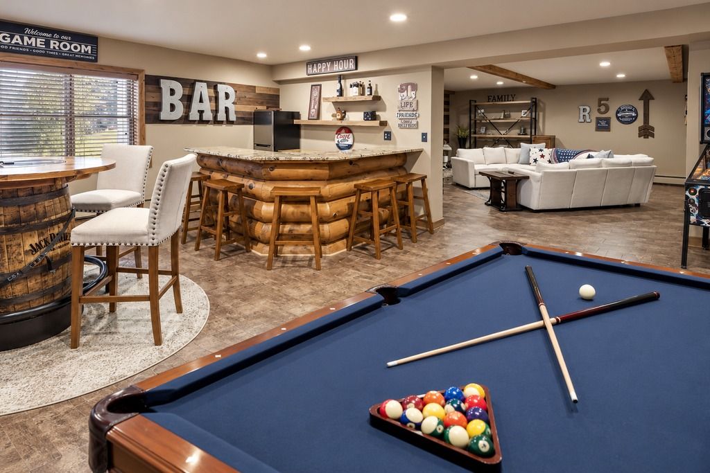 A pool table with billiard balls, a bar area with stools, a pool table, and a sofa in a room with a wooden floor.