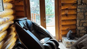 En stuga med träpanel på insidan, komplett med massagestol, en vägg av sten och utsikt över naturen.