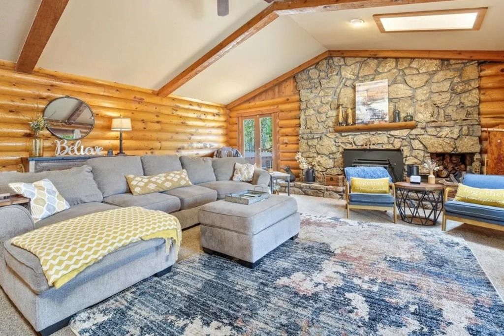 A log cabin interior with a stone fireplace, a sofa set, and a patterned rug.