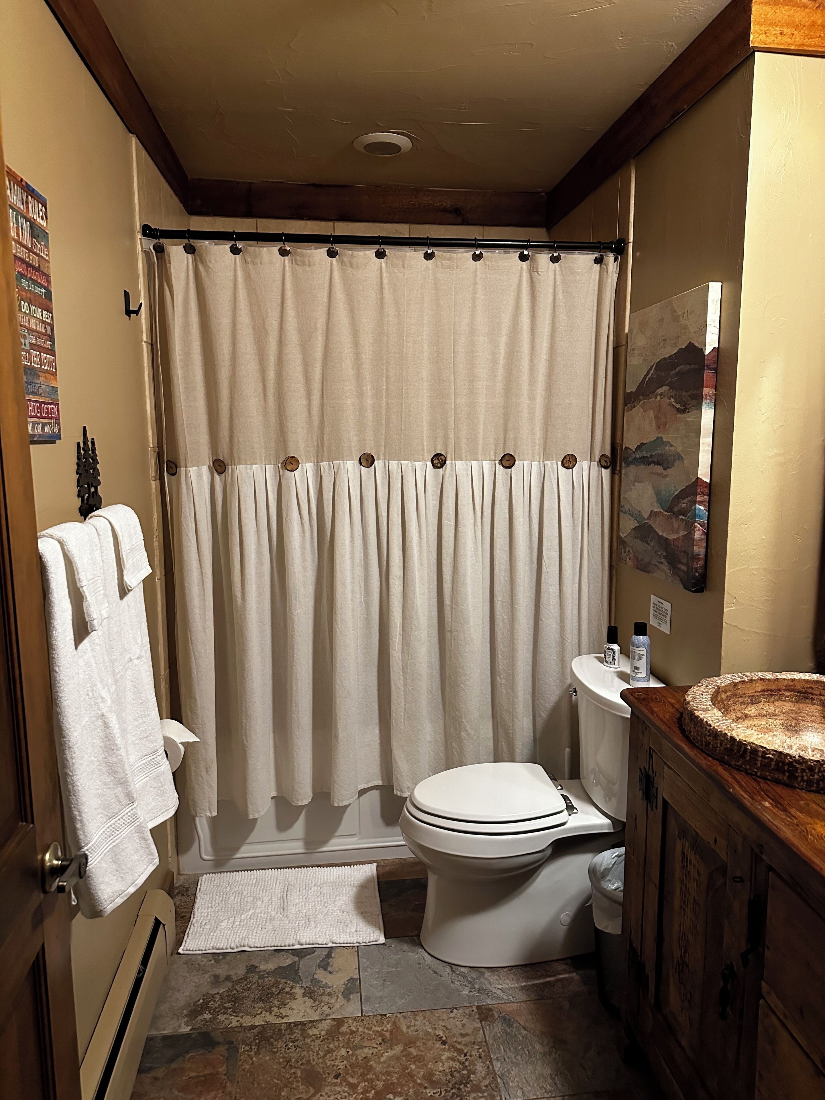 Un baño con cortina de ducha, inodoro, lavabo con recipiente decorativo y toallero.