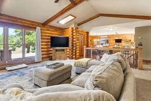 Interior de una cabaña de troncos con sala de estar, televisión, cocina y comedor.