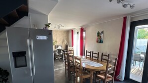 Una cucina moderna con frigorifero integrato, un'area pranzo con tavolo e sedie in legno, e un'ampia finestra con tende rosse.