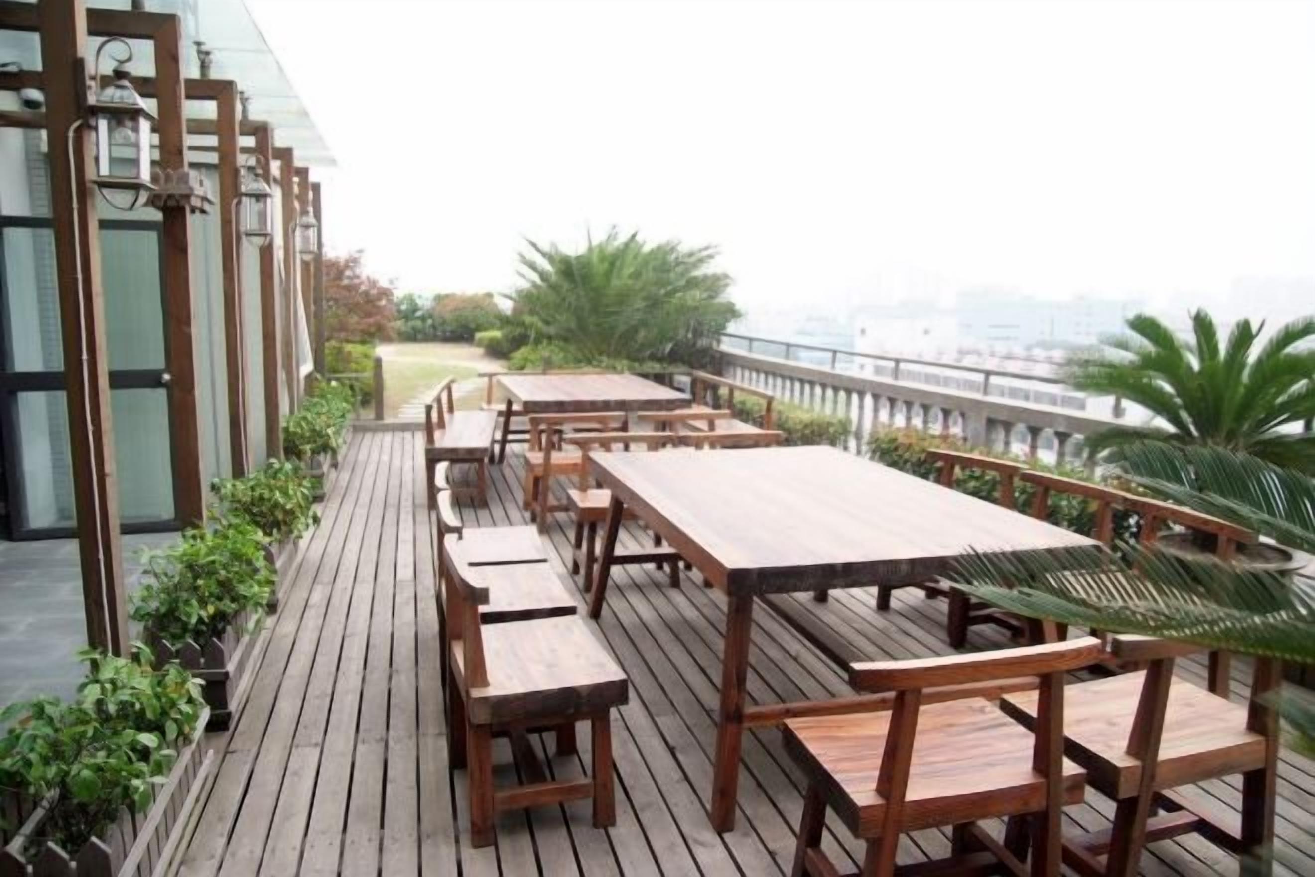 A rooftop terrace with wooden tables and benches, a view of the city, and a railing.