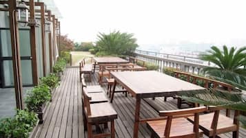A rooftop terrace with wooden tables and benches, a view of the city, and a railing.