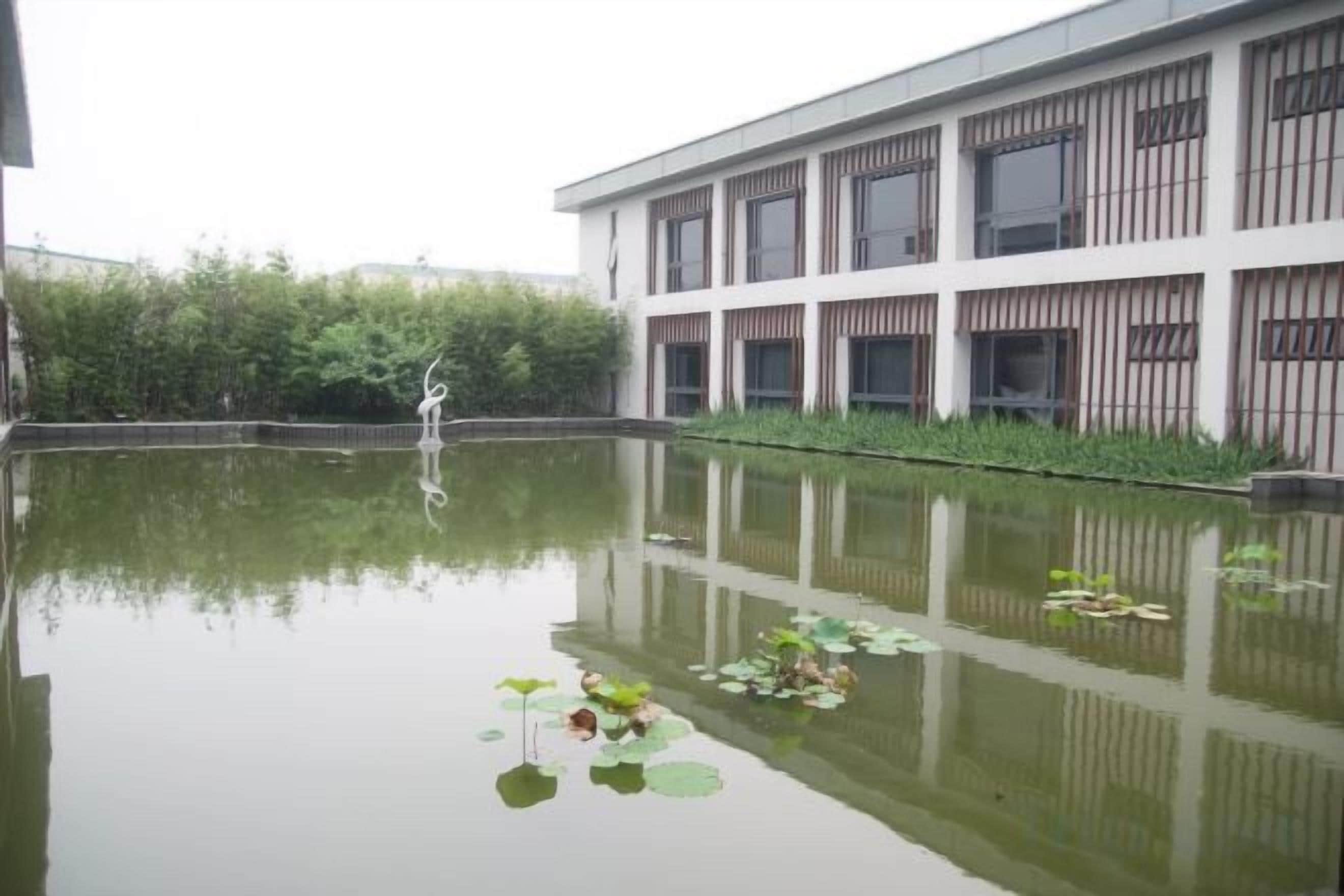 A building with a reflective water feature in front, surrounded by greenery.