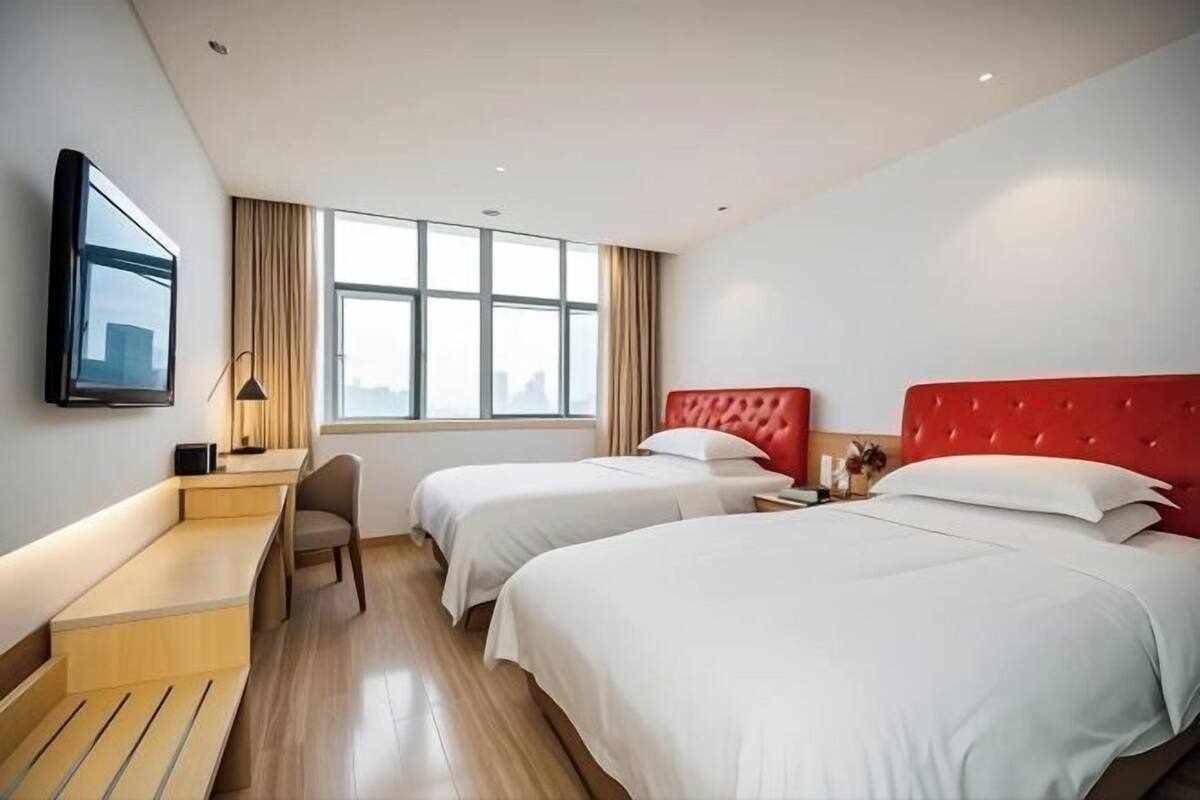 A hotel room with two beds, a desk, a chair, and a large window.