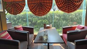 A room with a sofa set, a table, and a view of greenery through large windows.
