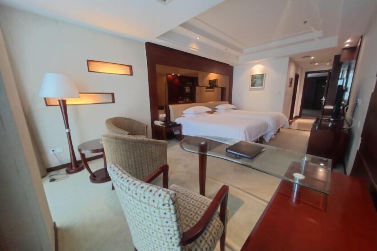 A hotel room with a bed, a chair, a desk with a laptop, a lamp, and a mirror.