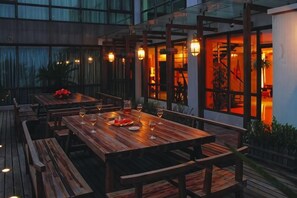 An outdoor dining area with wooden tables and benches, ambient lighting, and a view of the interior through glass doors. - ShangHai NvYan Hotel (Shanghai)