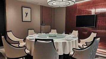 A conference room with a round table, white chairs, a television on the wall, and a framed picture.