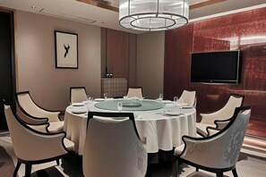 Un salón de conferencias con una mesa redonda, sillas blancas, un televisor en la pared y un cuadro enmarcado.