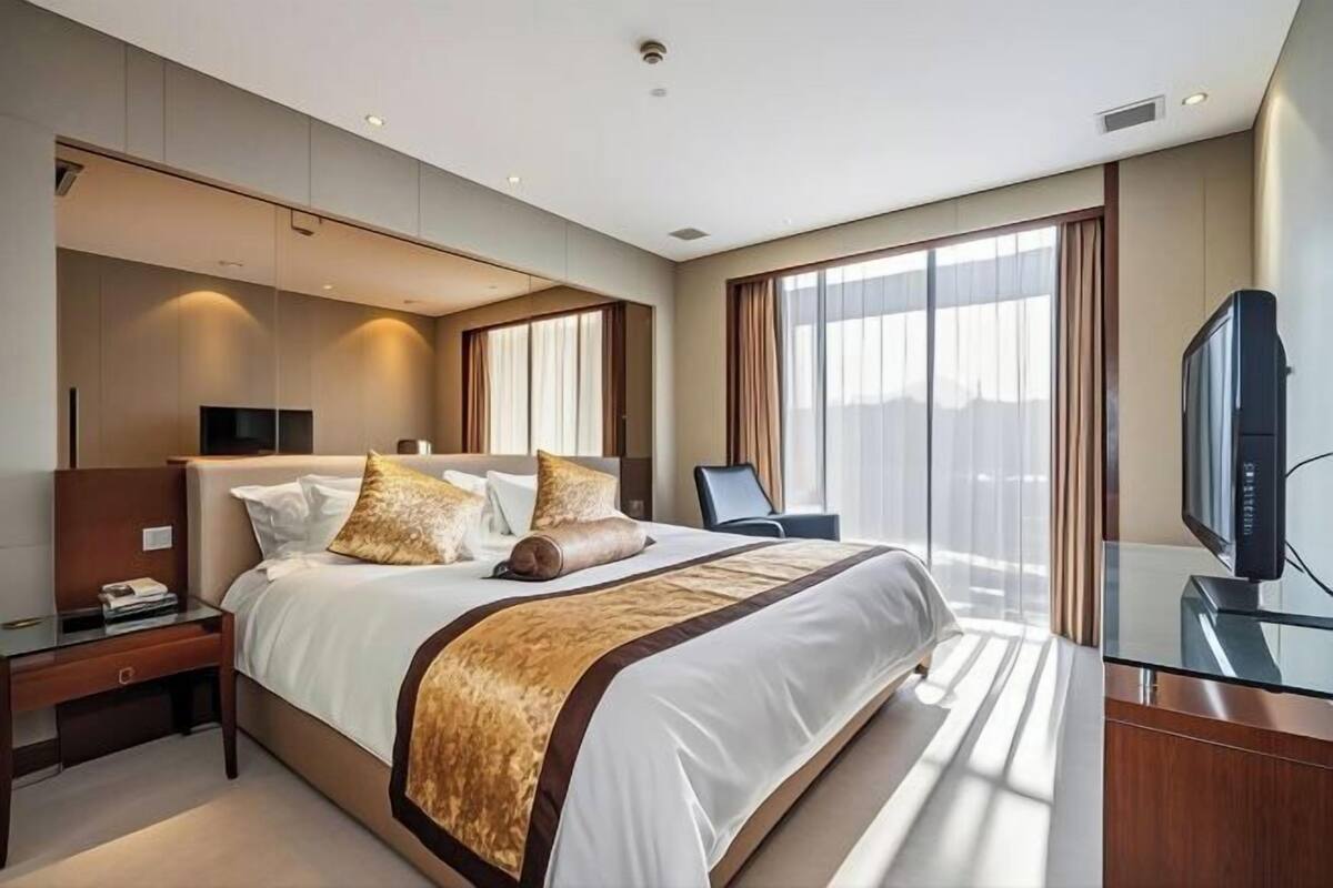 A modern hotel room with a large bed, a desk, a television, and a large window.