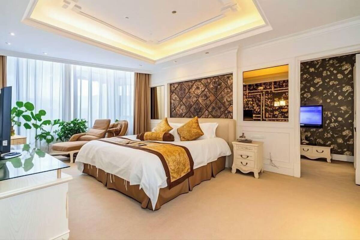 A modern hotel room with a large bed, a TV, a desk, and a seating area.