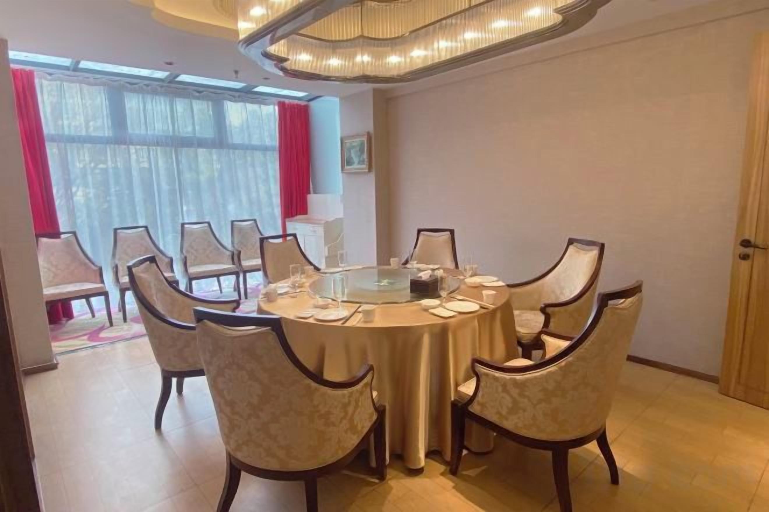 Un comedor con una mesa redonda rodeada de sillas, una araña y vistas amplias a través de grandes ventanales.