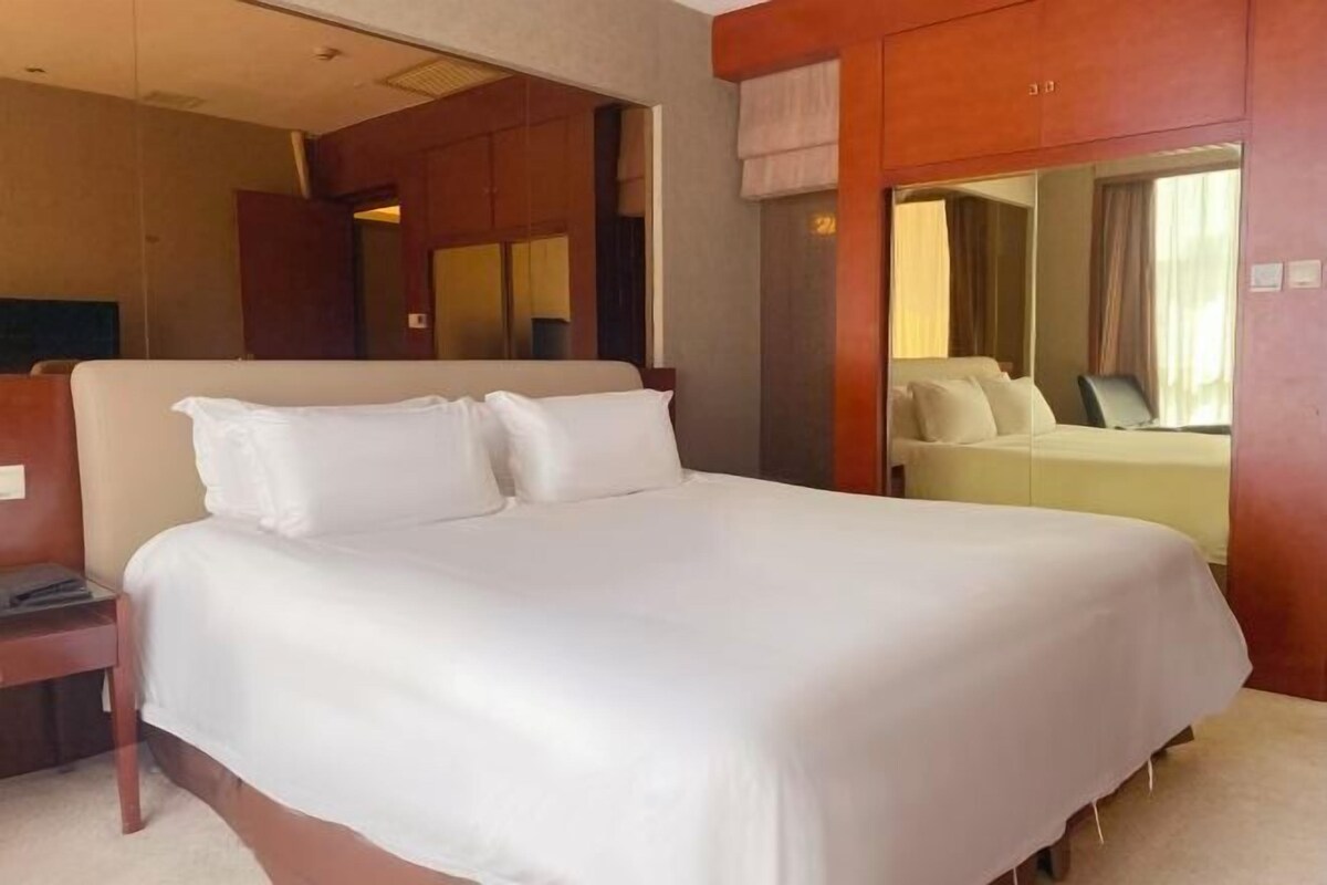A hotel room with a large bed, a bedside table, a mirror, and a window with curtains.