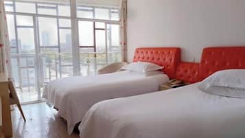 A hotel room with two beds, a wooden desk, and a large window offering a city view.