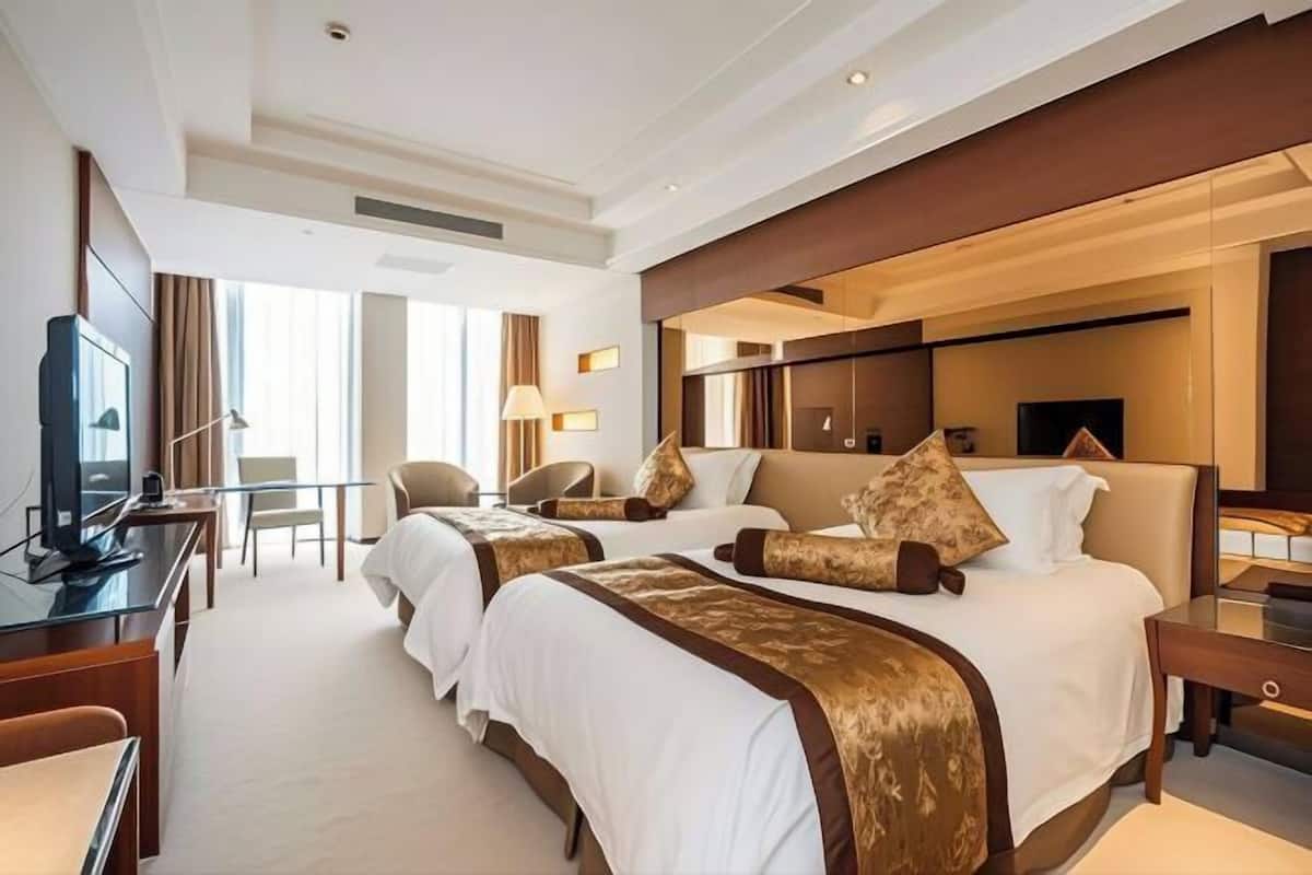 A hotel room with two beds, a desk, a chair, and a television.
