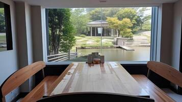 A dining area with a wooden table and chairs, a view of a garden and pond through large windows.