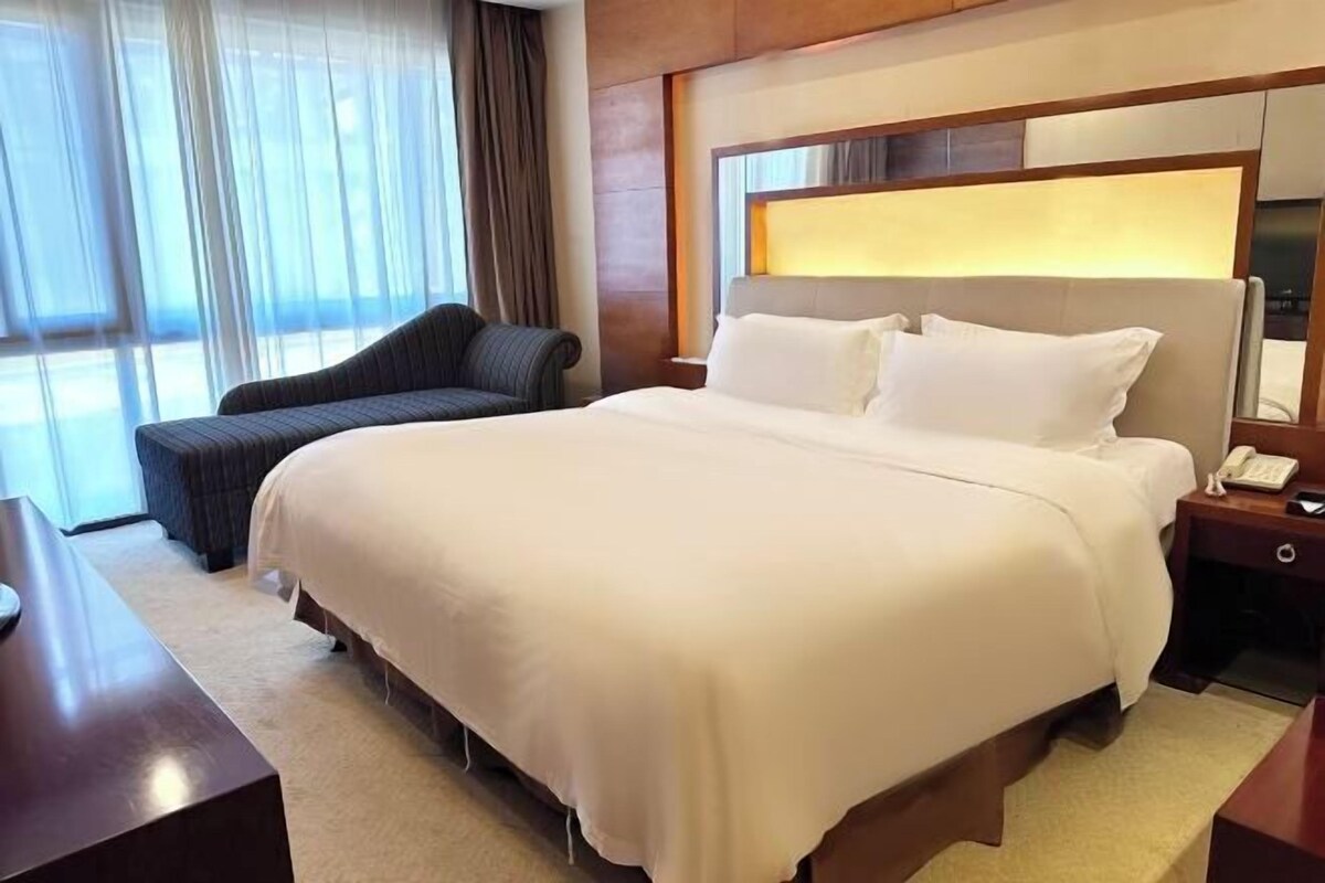 A hotel room with a large bed, a bedside table with a phone, and a window with curtains.