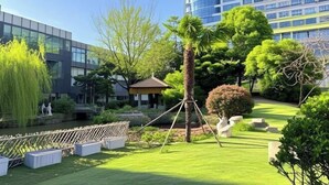 Un patio bien cuidado con un estanque, abundante vegetación y edificios modernos al fondo.
