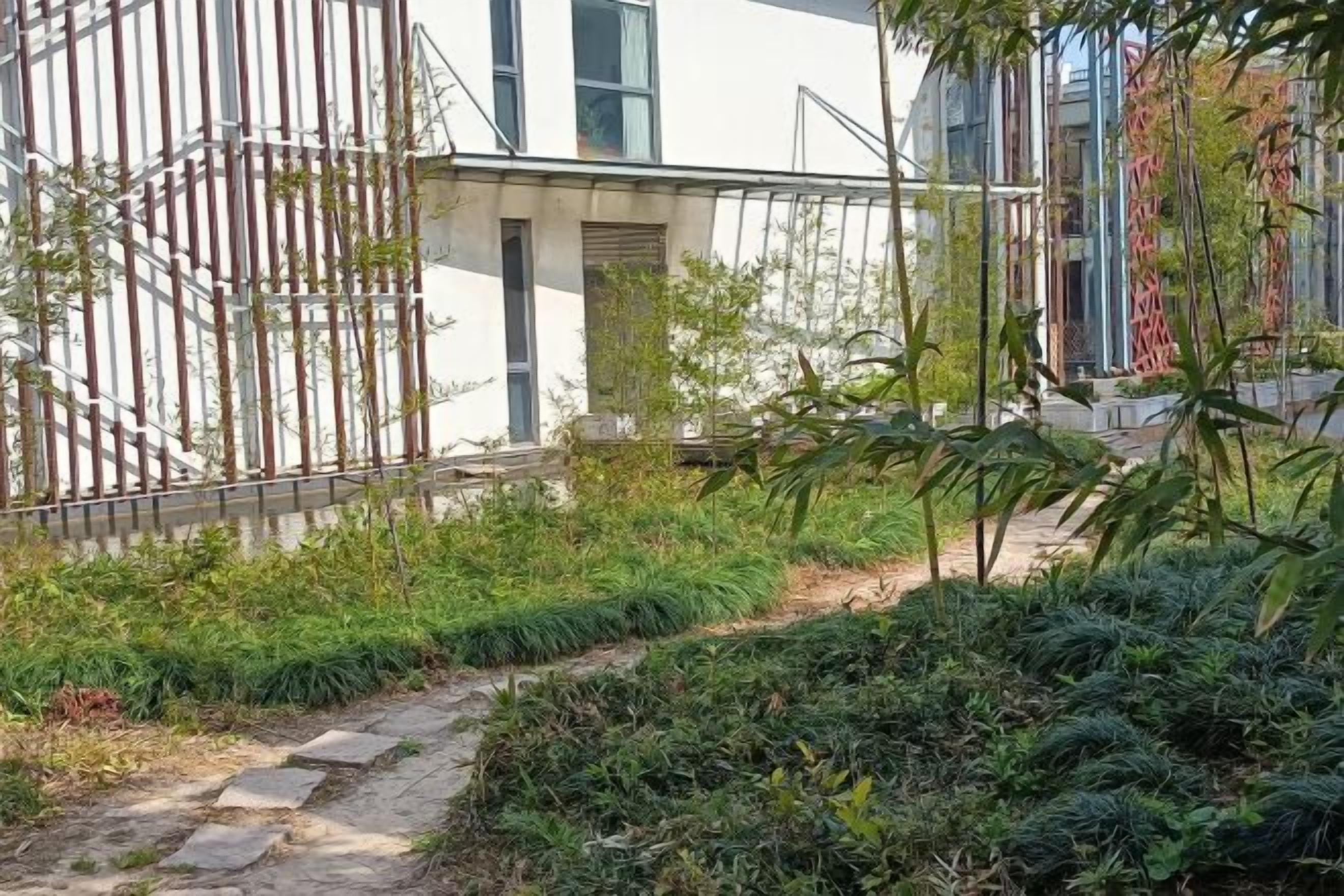 Un sendero conduce a un edificio de diseño moderno, rodeado de vegetación y una valla metálica.