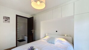 Ein ordentlich bezogenes Bett mit weißen Leinen und einem Handtuch, eine Nachttischlampe sowie eine Tür zu einem Badezimmer.
