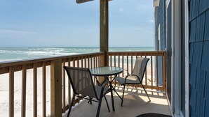Une terrasse en bois avec une table et des chaises en verre, donnant sur une plage.