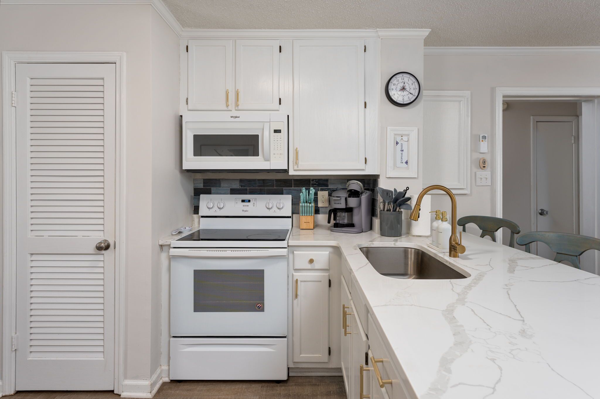 A kitchen with white cabinetry, a microwave, an oven, a sink, and a clock on the wall.