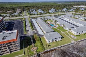 An aerial view of a resort with multiple buildings, a parking lot, and a beach area. - Sun Beach Club 2BR Closest Building to Beach Access with Covered Patio (New Smyrna Beach)